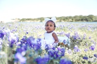 a baby girl sitting in a field of bluebonnets